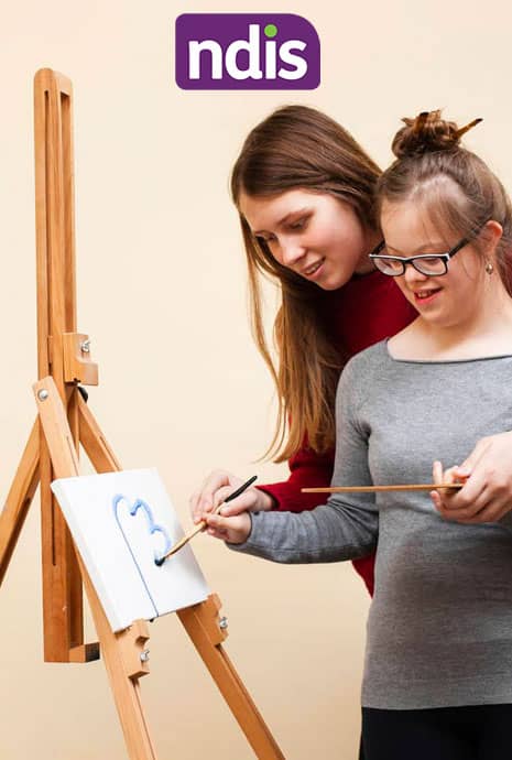 Two women creating art on an easel with a painting board, supported by NDIS services.